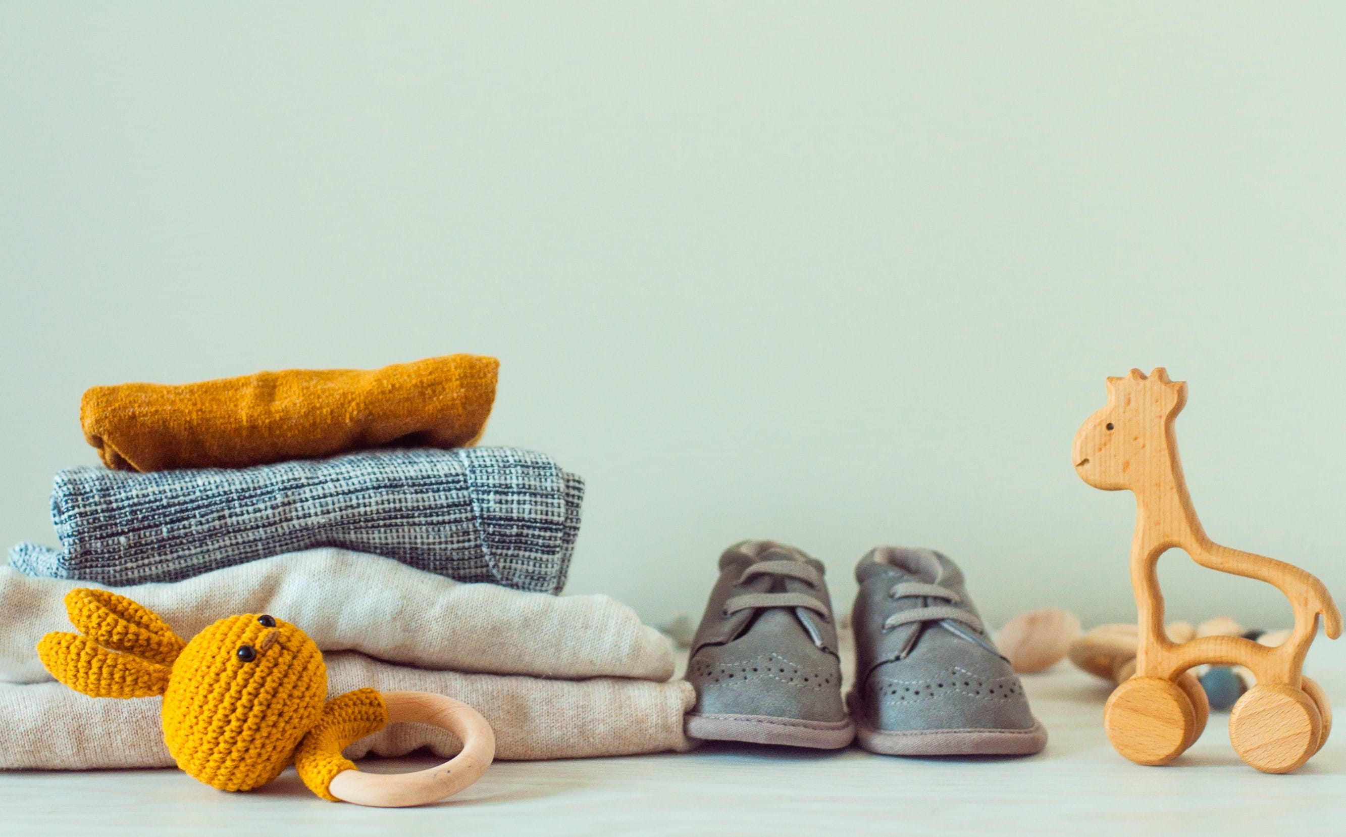 baby clothes folded up with shoes next to it and small toys in the foreground